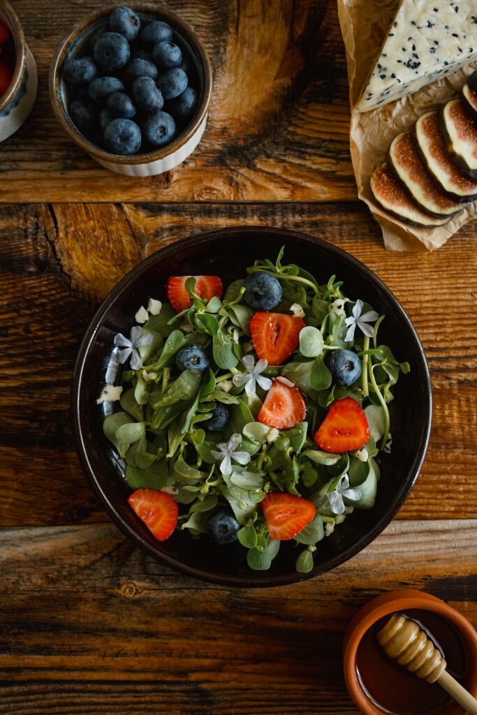 Top view of a fresh salad with strawberries, blueberries, and flowers on a rustic table.